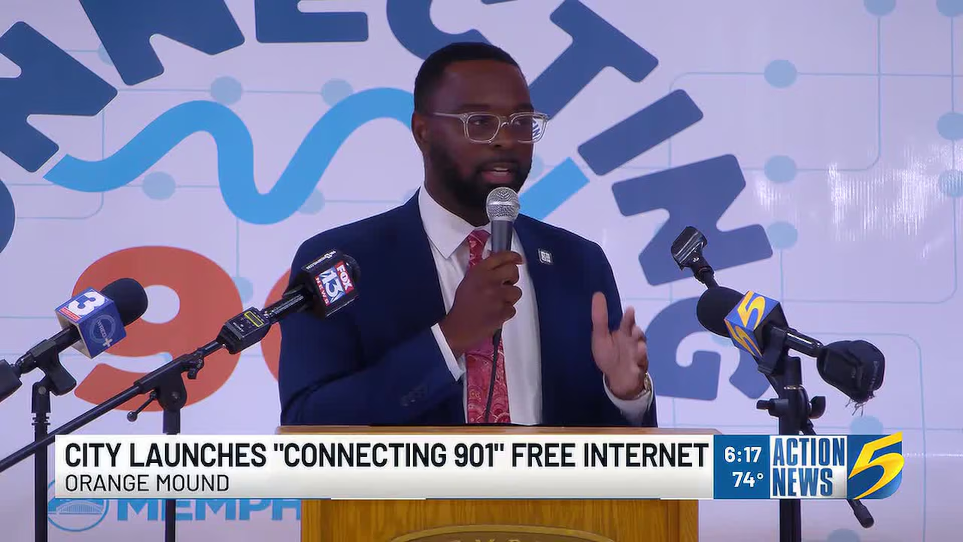 A speaker at the Connecting 901 launch, with local news microphones at the podium.